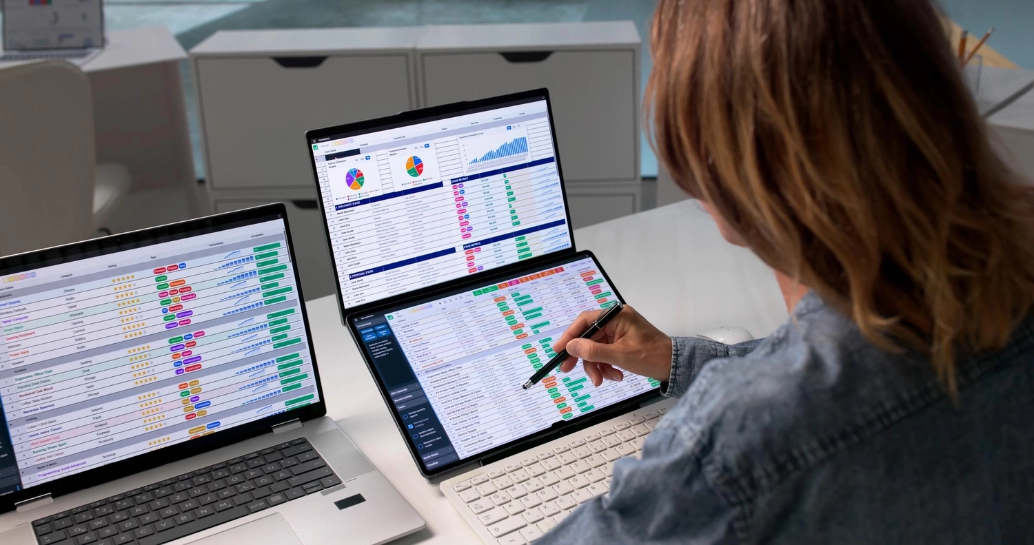 Neoflex – Kaufmännische Dienstleistungen & Betreuung – Eine Person, die an einem Schreibtisch mit zwei Laptops und einem Tablet mit zwei Bildschirmen sitzt und farbenfrohe Diagramme, Grafiken und Daten-Dashboards analysiert.
