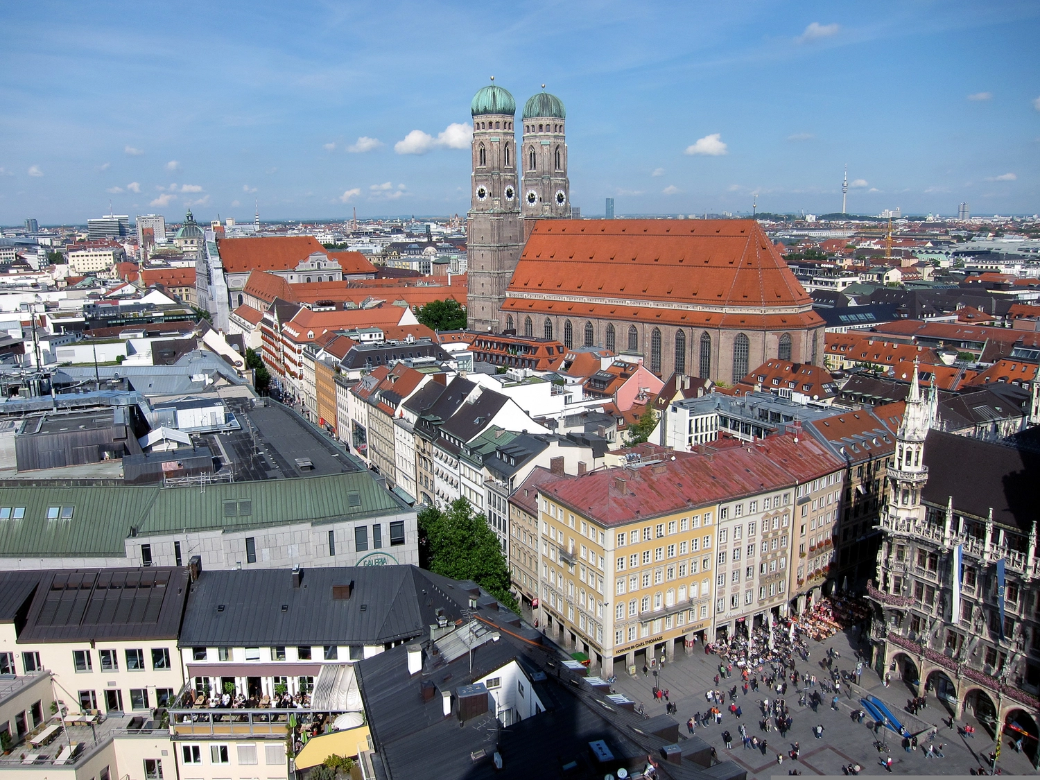 Neoflex – Kaufmännische Dienstleistungen & Betreuung – Eine Luftaufnahme der Münchner Innenstadt, auf der die Frauenkirche mit ihren roten Dächern und ihren beiden Zwillingstürmen zu sehen ist, die sich über historische Gebäude und den belebten Marienplatz erheben.
